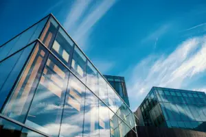 Modern glass buildings reflecting clouds against a clear blue sky, symbolizing Trust PC Expert's innovative IT solutions and professional services.